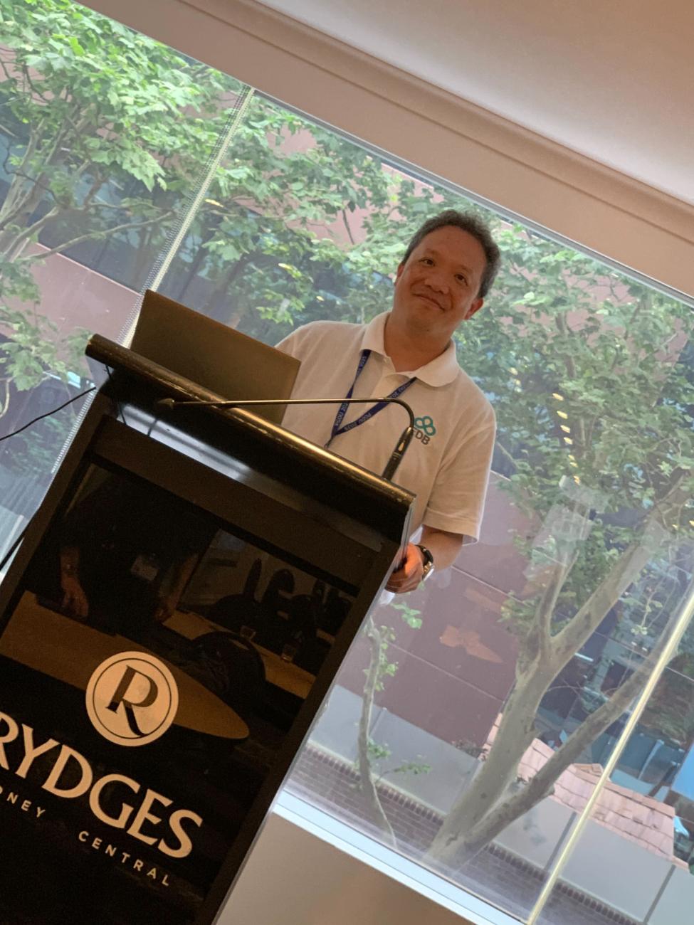 Mark Wong at Postgres Down Under, behind the speaker desk