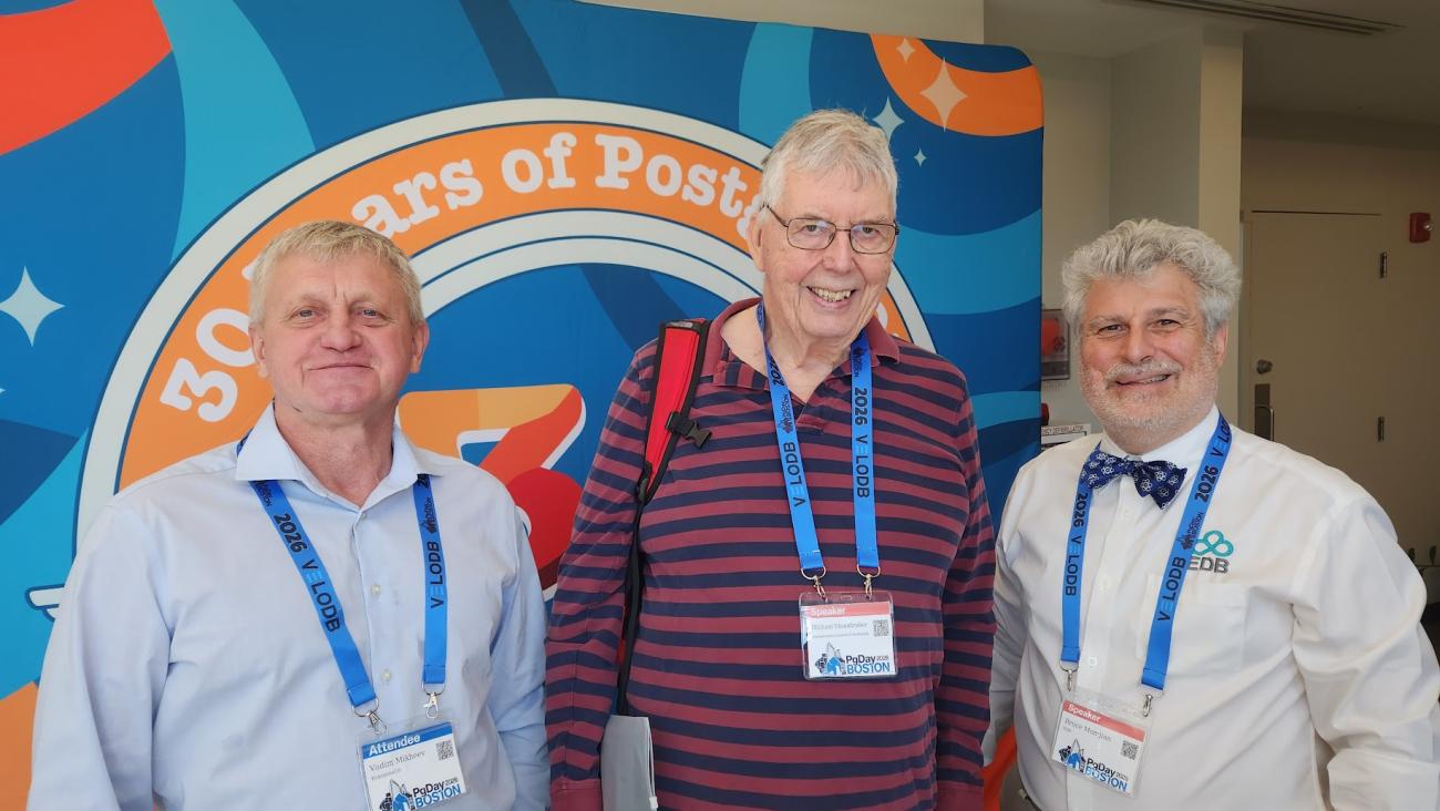 Vadim Mikheev, Michael Stonebraker and Bruce Momjian pose for a picture in front of the 30 years of PostgreSQL banner